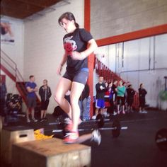 a woman riding a skateboard on top of a wooden box in a gym filled with people