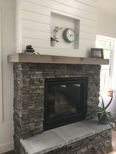 a stone fireplace with a clock on the wall above it and a potted plant