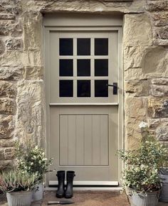 a pair of black rubber boots sitting in front of a stone building with two planters