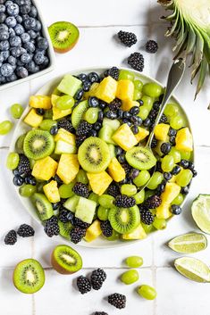 a white plate topped with kiwis, blueberries and blackberries next to a pineapple