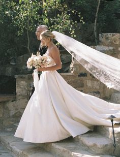 the bride and groom are walking down the steps together in their wedding dress, veil blowing in the wind