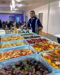 a man standing in front of a table filled with trays of different types of food