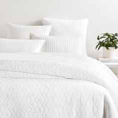 a bed with white sheets and pillows in a room next to a potted plant