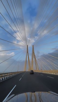 a car driving across a bridge with many cables in the sky over it's head