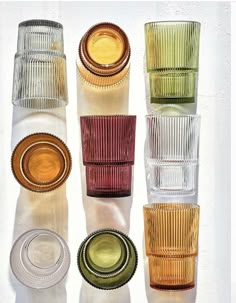 several different colored glass cups and saucers on a white surface with shadows from them