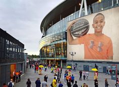 a large group of people walking in front of a building with a giant advertisement on it