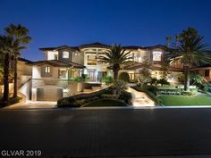 a large house is lit up at night with palm trees in the front yard and landscaping