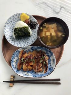 two plates with food on them and chopsticks next to one bowl of soup