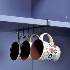 three coffee mugs hanging from hooks on a shelf in a room with blue walls