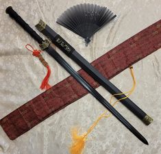 two black and red japanese style swords, one with an orange tassel, the other with a fan