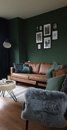 a living room with dark green walls and leather couches in the corner, while other furniture sits on top of a hard wood floor