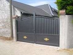 an iron gate in front of a grey house with two gold designs on the sides