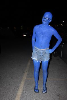 a man with blue paint on his body standing in the middle of the road at night