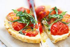 two small pizzas with tomatoes and basil on them are cut in half to eat