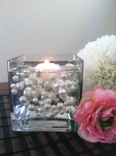 a candle that is sitting on a table next to flowers and a vase with some pearls in it