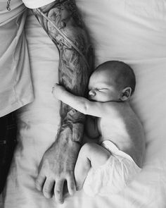 a man holding a baby on top of a bed next to a person with tattoos