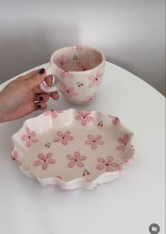 a hand holding a coffee cup next to a pink flowered bowl on a white table