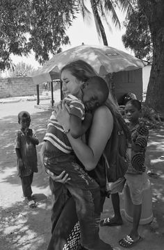 black and white photograph of two people hugging each other in front of a group of children under an umbrella