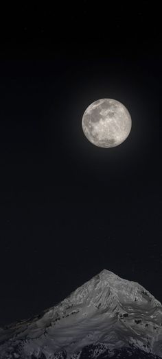 the full moon is seen over a snowy mountain