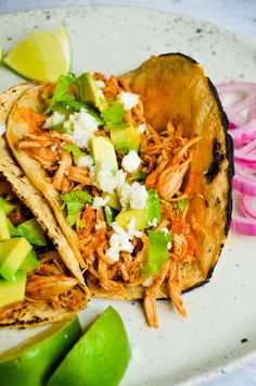 two tacos with shredded meat, avocado and cilantro on a plate