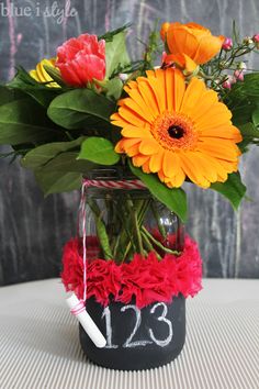 an arrangement of flowers in a vase with a chalkboard sign on the side that says 123