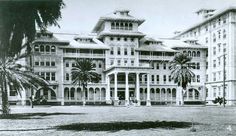 an old black and white photo of a large building with palm trees in front of it