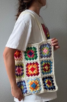 a woman holding a multicolored crocheted bag