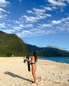 a woman walking on the beach carrying a surfboard