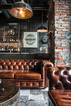 a living room filled with brown leather couches next to a brick wall and bar