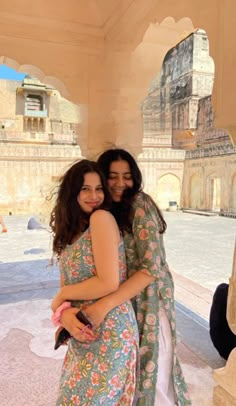 two women standing next to each other in front of a stone building with arches and pillars