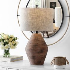 a table with a lamp, vase and mirror on it in front of a round mirror