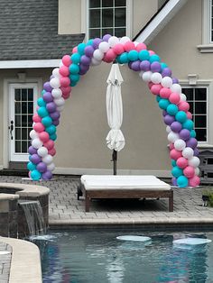 an arch made out of balloons over a swimming pool with a chaise lounge in the foreground