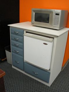 a microwave oven sitting on top of a white and blue cabinet next to an orange wall