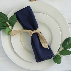 a place setting with blue napkins and green leaves on the plate, next to a cookie