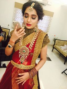 a woman in a red and gold bridal outfit looking at her cell phone