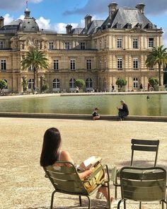 a woman is sitting on a chair in front of a large building with a fountain