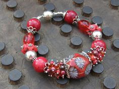 "Centerpiece in this striking scarlet bracelet is a large chunky lampwork bead, surrounded by a variety of gemstones, including Coral, Red garnet, freshwater pearls, faceted Redwine Quartz, sparkling Swarovski crystals and Sterling silver. It closes with a Sterling silver magnetig clasp. Length 19cm/ 7.48\" You can find more of our bracelets here: https://www.etsy.com/nl/shop/VonCliecXclusives?section_id=14028198&ref=shopsection_leftnav_2" Red Czech Glass Bracelet With Round Beads, Handmade Red Glass Beaded Bracelets, Red Czech Glass Bracelet, Red Coral Jewellery, Cluster Bracelet, Coral Beads Necklace, Cluster Bracelets, Bali Silver, Unique Holiday Gifts