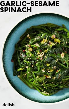 a blue bowl filled with green vegetables on top of a white countertop and the words garlic sesame spinach