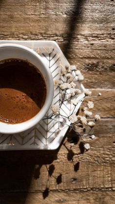 a cup of coffee sitting on top of a white saucer next to dried flowers