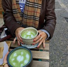 a woman sitting on a bench holding a bowl of green liquid