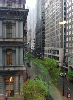 a city street filled with tall buildings and lots of green trees in the foreground