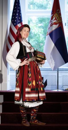 a woman dressed in traditional clothing standing next to two flags and an american flag behind her