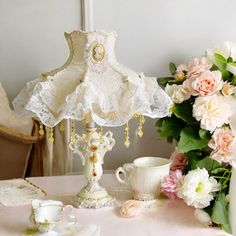 a table topped with a lamp next to a vase filled with pink and white flowers