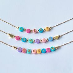 Add a burst of vibrant charm to your little one's outfit with our Bright Colorful Beads Name Necklace! This delightful piece combines the timeless elegance of dainty gold name beads with an array of eye-catching, colorful hued beads. Each letter of your child's name is lovingly crafted with precision and adorned with a captivating spectrum of colors, creating a personalized gift that will surely bring smiles. These necklaces would also make great party favors for a childs birthday party. Beads are chosen randomly and the necklace is accented with 18K gold hearts or 18K round ball beads.  Necklace chain is 18K plated and dainty.  Choose which style you would like from the drop down menu along with the length of the necklace. Necklace is packaged for gift giving. To see more Kids Necklaces c Playful Beaded Charm Necklaces For Gifts, Playful Beaded Charm Necklaces As Gifts, Playful Beaded Charm Necklace For Gifts, Sweet Beaded Jewelry For Birthday, Cute Personalized Multicolor Charm Necklaces, Playful Beaded Jewelry For Mother's Day, Playful Heart-shaped Letter Beads Bracelet, Personalized Playful Necklace For Friendship, Valentine's Day Playful Beaded Jewelry