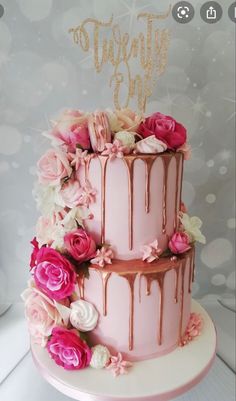 a three tiered cake with pink and white flowers on the side, topped with a gold topper