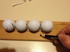 four white golf balls are lined up on a wooden board with a marker in the foreground