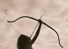 a woman holding onto a bow while standing on top of a hill with her hands in the air