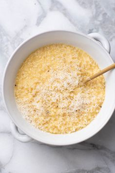 a white bowl filled with cheese on top of a marble counter next to a wooden spoon