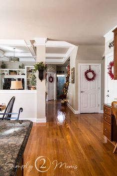 a kitchen and dining room are decorated for christmas with wreaths on the door, potted plants in pots, and wood floors