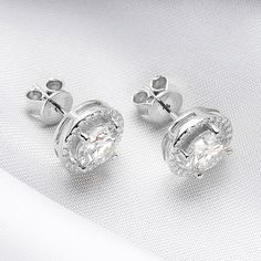 Experience the timeless elegance of a Classic 2.0 Carat Round Cut Moissanite Stud Earrings from Evani Naomi Jewelry. These high-quality earrings are simply stunning in their design and craftsmanship. Their brilliant shine is much like that of a mined diamond but comes at a significantly more affordable price. Each stud is finely handcrafted to last a lifetime, offering you a timeless piece to enjoy for years to come. They are made from a blend of 92.5% pure silver + 7.5% hypoallergenic metals an Silver Moissanite Halo Diamond Earrings, Silver Moissanite Diamond Earrings With Halo Design, Silver Moissanite Earrings With Halo Design, White Gold Moissanite Halo Earrings, Timeless Cluster Earrings With Brilliant Cut Cubic Zirconia, Elegant Round Cluster Earrings With Lab Grown Diamonds, Elegant Lab Grown Diamond Cluster Earrings As Gift, Elegant Lab Grown Diamond Cluster Earrings For Gifts, Timeless Bridal Earrings With Diamond Cut Cubic Zirconia